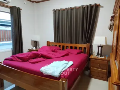 Cozy bedroom with wooden furniture and vibrant red bedding, perfect for relaxation and comfort.