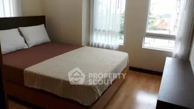 Cozy bedroom with large windows and wooden flooring in modern apartment.