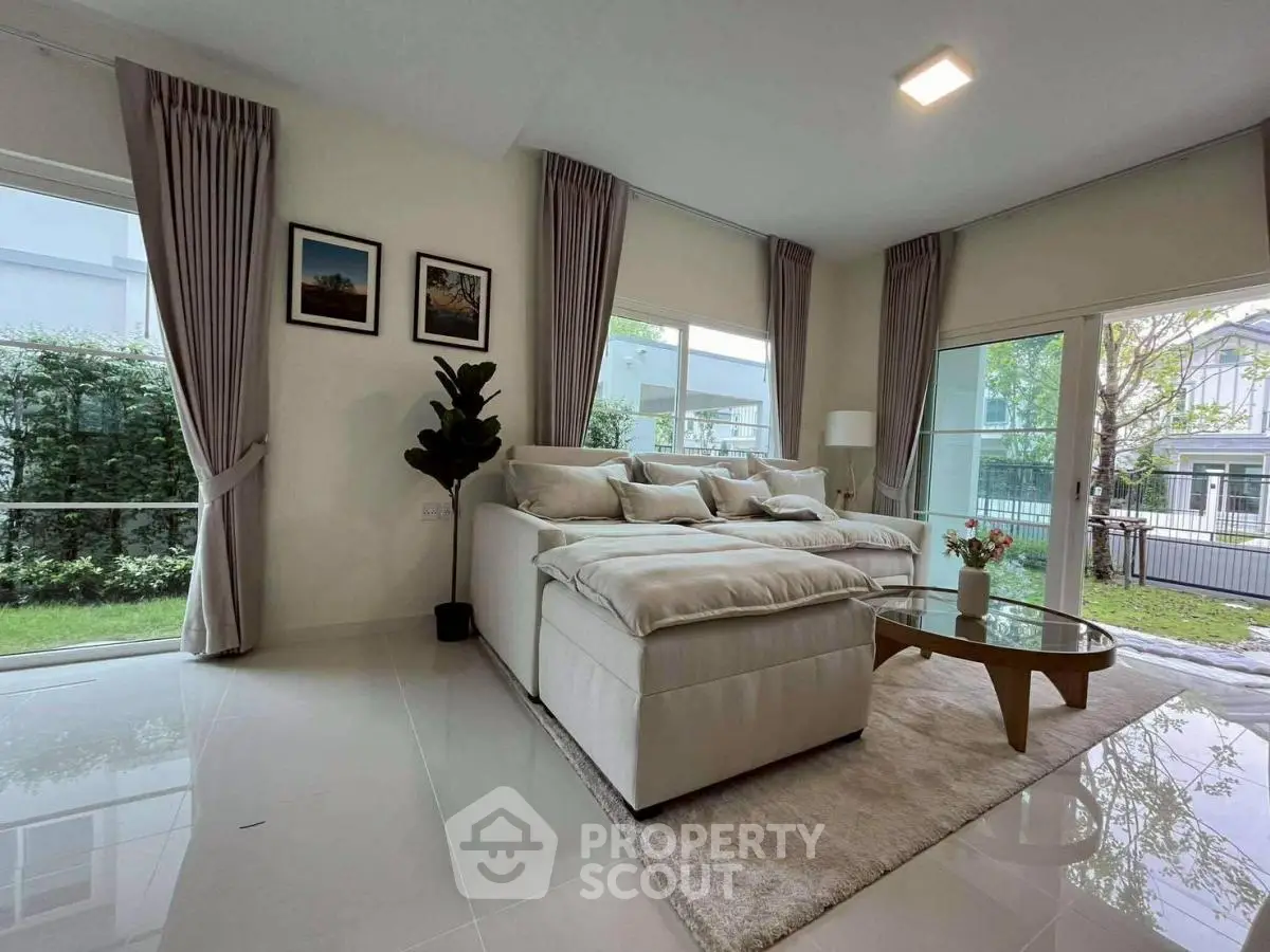 Spacious modern living room with large windows and garden view, featuring elegant decor and natural light.