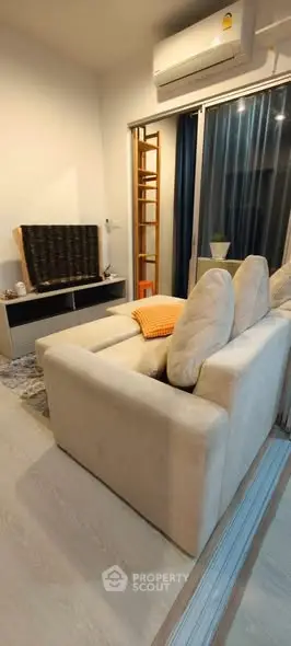 Cozy living room with modern sofa and air conditioning, featuring a sleek entertainment unit and sliding glass doors.