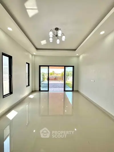 Spacious living room with modern chandelier and large windows opening to a balcony with scenic view.