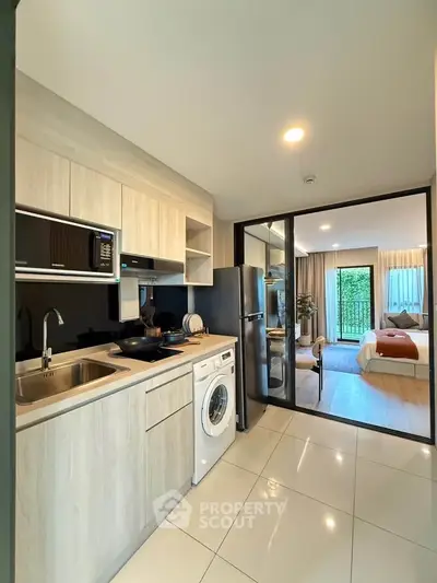 Modern open-layout kitchen with washing machine and view into cozy bedroom
