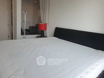 Spacious bedroom with modern decor and large bed, featuring a stylish red lamp and sleek black headboard.