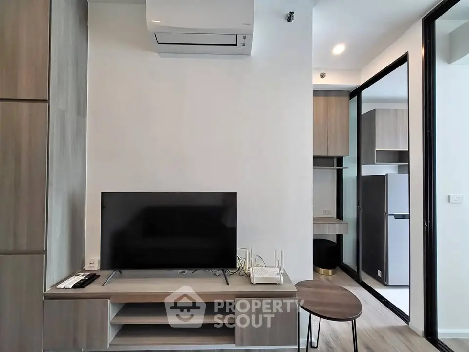 Modern living room with sleek TV setup and open kitchen layout in stylish apartment.