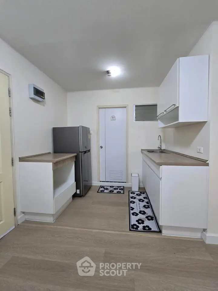 Modern kitchen with sleek white cabinets and stainless steel fridge in a compact layout.