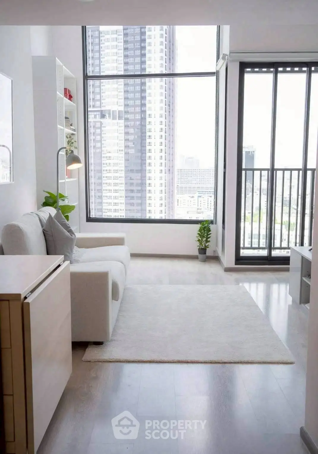Modern living room with large windows and city view, featuring cozy white sofa and sleek decor.