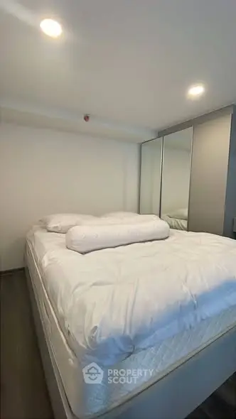 Cozy bedroom with plush bedding and mirrored wardrobe in modern apartment.
