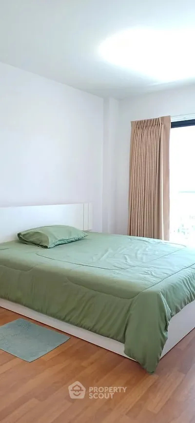 Bright and cozy bedroom with green bedding and wooden flooring, perfect for relaxation.