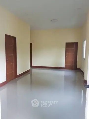 Spacious empty room with glossy floors and wooden doors, ideal for customization.