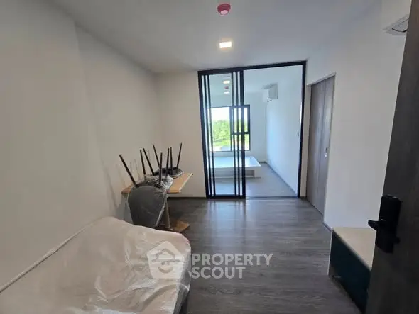 Modern apartment interior with sleek flooring and sliding glass doors leading to a bright balcony view.