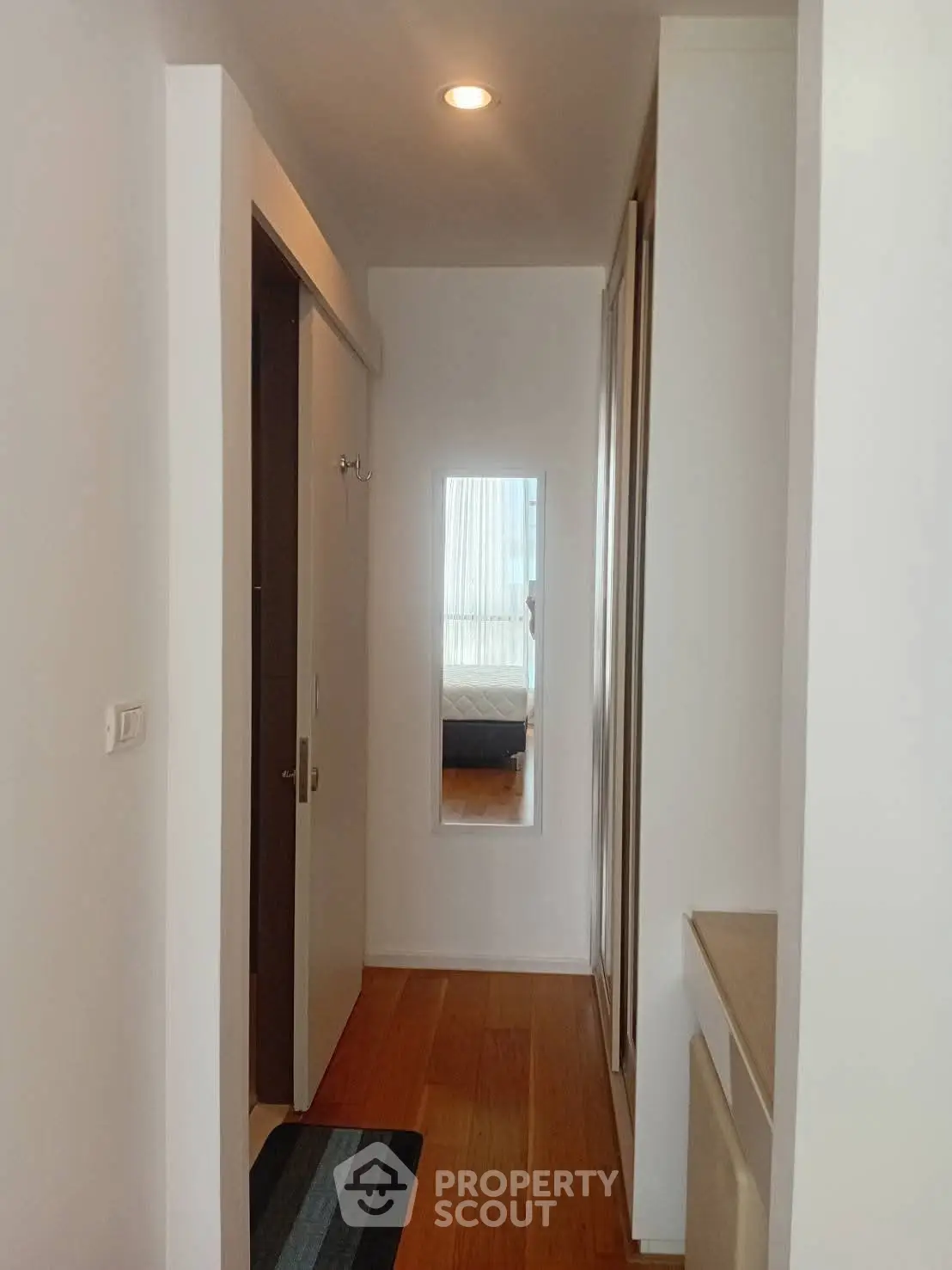 Modern hallway with wooden flooring leading to a cozy bedroom, featuring sleek design and ample natural light.