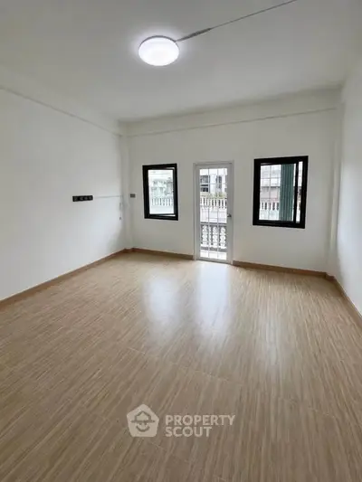 Spacious empty room with wooden flooring and large windows for natural light.