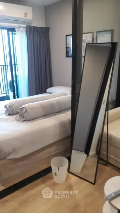 Modern bedroom with stylish decor and floor-to-ceiling mirror, featuring cozy bedding and natural light.