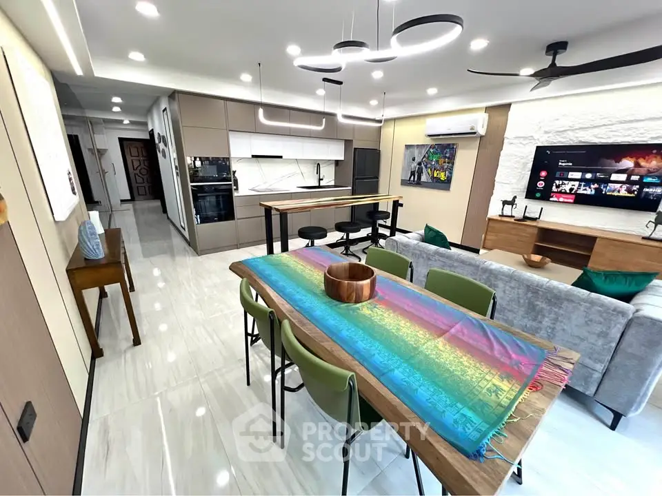 Modern open-plan living room with stylish kitchen and dining area, featuring sleek furniture and vibrant decor.