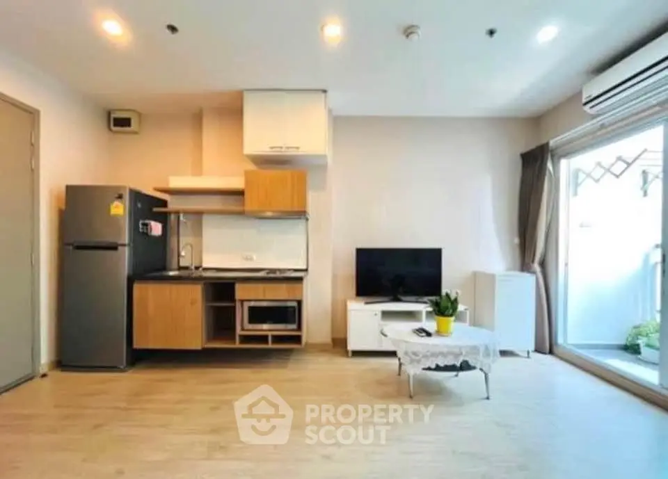 Modern open-layout living room with kitchen, featuring wooden flooring and natural light.