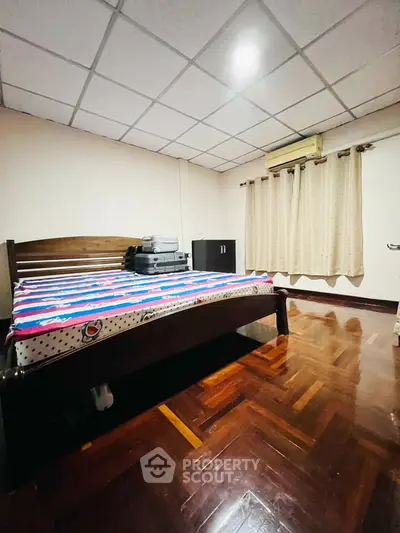 Cozy bedroom with wooden flooring and air conditioning, featuring a comfortable bed and ample natural light.