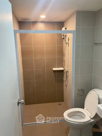 Modern bathroom with walk-in shower and toilet in a sleek tiled design.