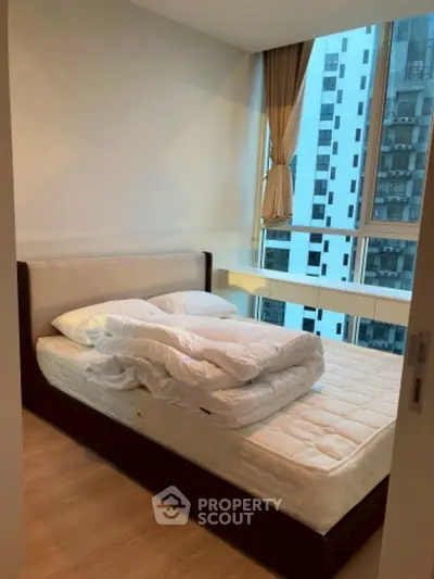 Cozy bedroom with large window offering city view in modern apartment.