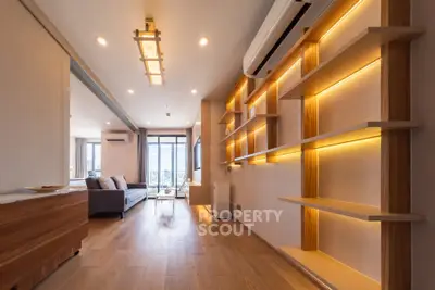 Spacious modern living room with wooden flooring and built-in shelves, featuring large windows and stylish lighting.