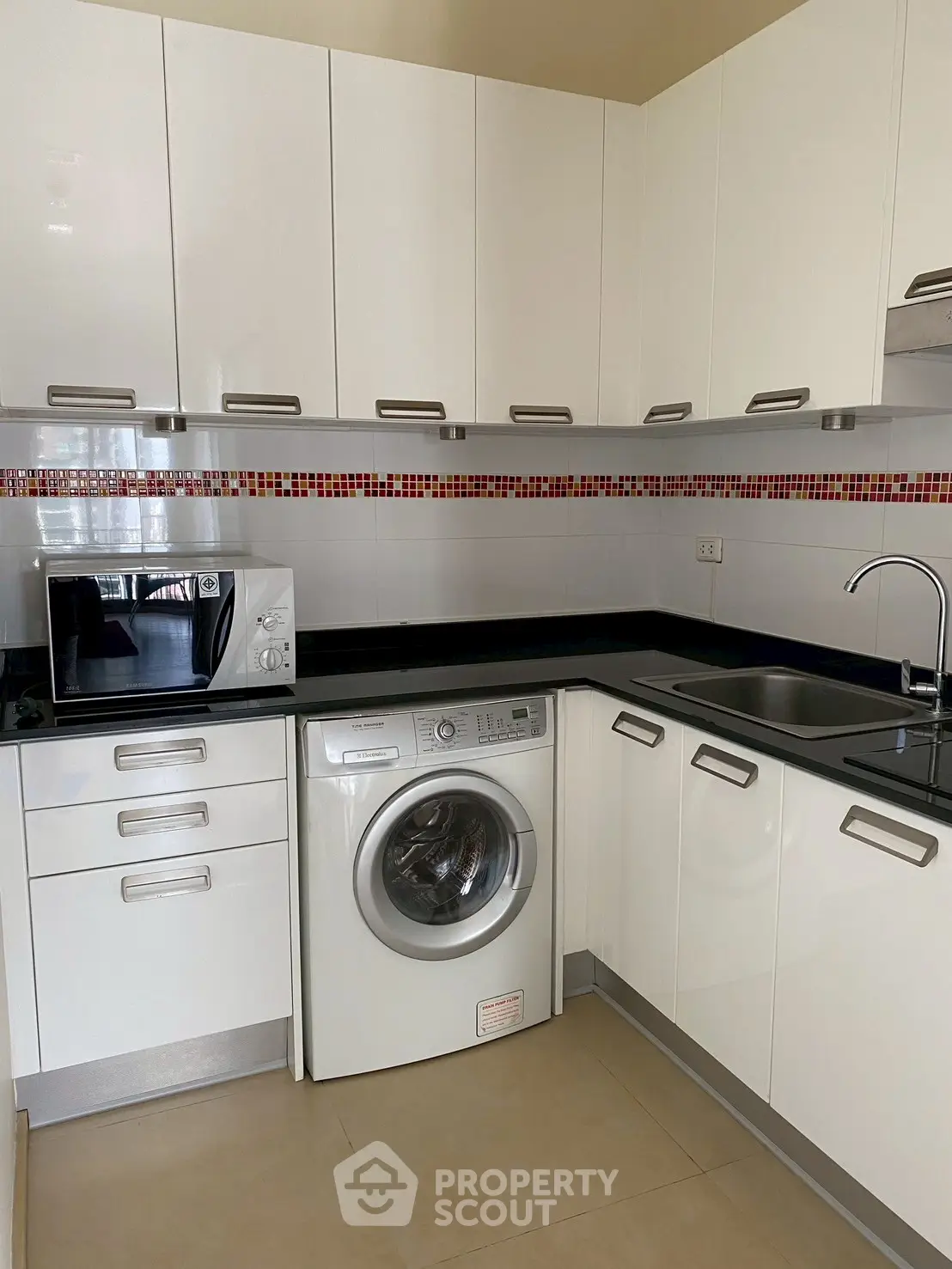 Modern kitchen with sleek cabinets, washing machine, and microwave in a compact layout.