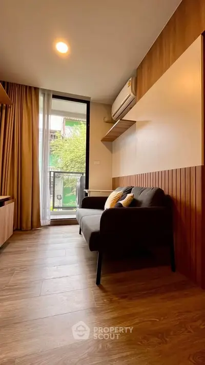 Modern living room with wooden flooring and balcony view, featuring a cozy sofa and air conditioning.