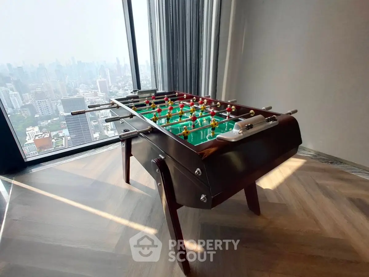 Luxurious high-rise apartment with stunning city view and stylish foosball table in living area.