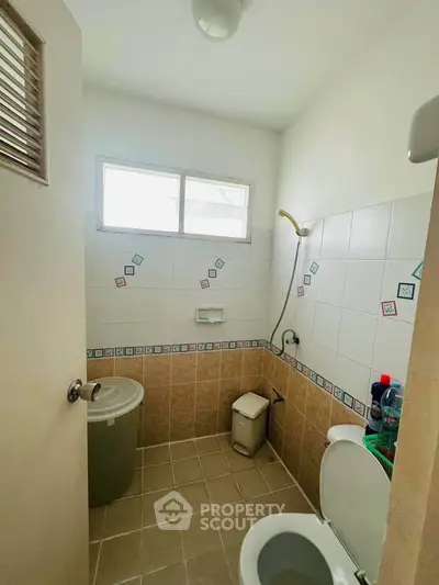 Compact bathroom with shower and toilet, featuring tiled walls and a small window for natural light.