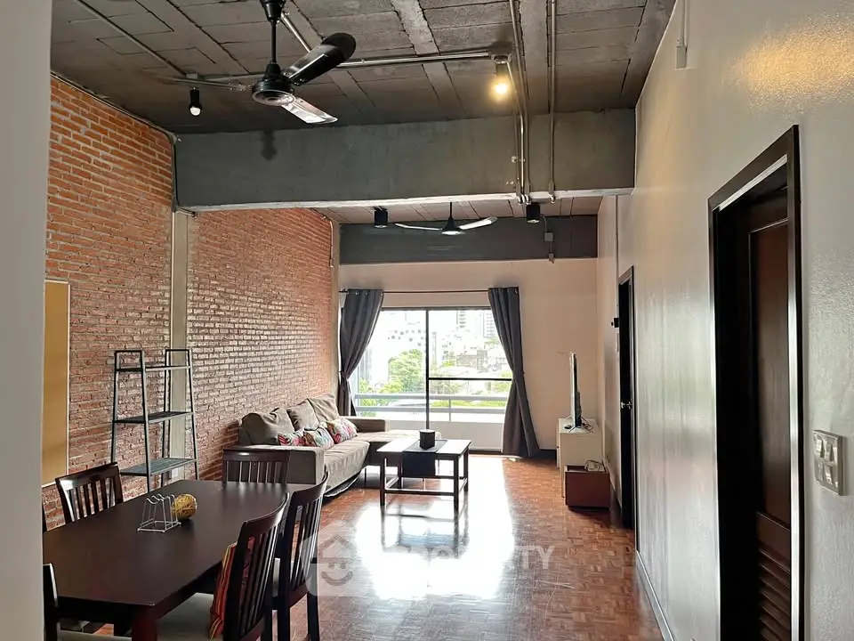 Spacious industrial-style living room with exposed brick and large windows offering city views.