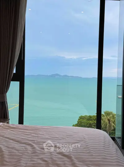 Stunning ocean view from a bedroom with large windows and elegant curtains.