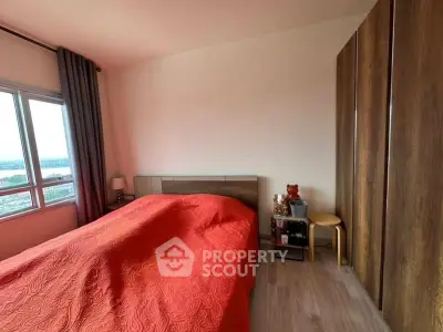 Cozy bedroom with large window and wooden wardrobe, featuring a vibrant red bedspread.