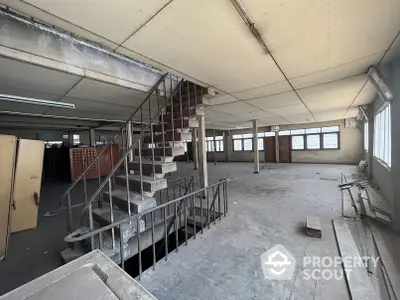 Expansive industrial loft space with high ceilings, large windows, and a sturdy staircase leading to a mezzanine level, ideal for a custom renovation.