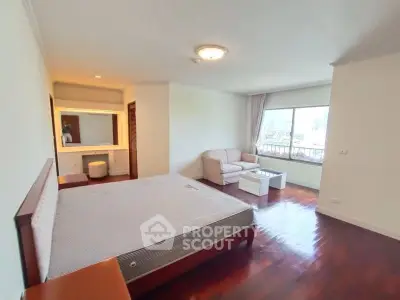 Spacious bedroom with city view, featuring a cozy seating area and elegant wooden flooring.