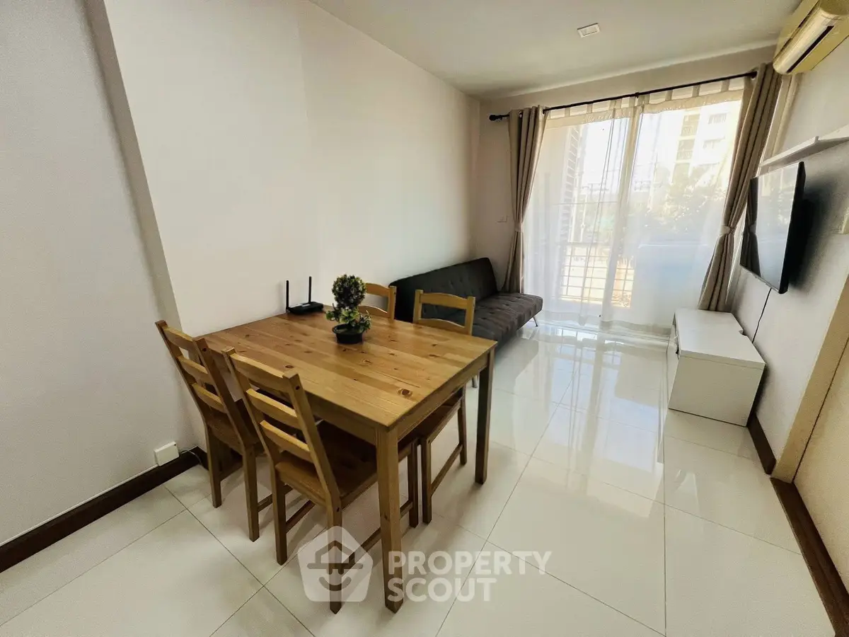 Modern living room with natural light, wooden dining set, and sleek TV setup in a stylish apartment.