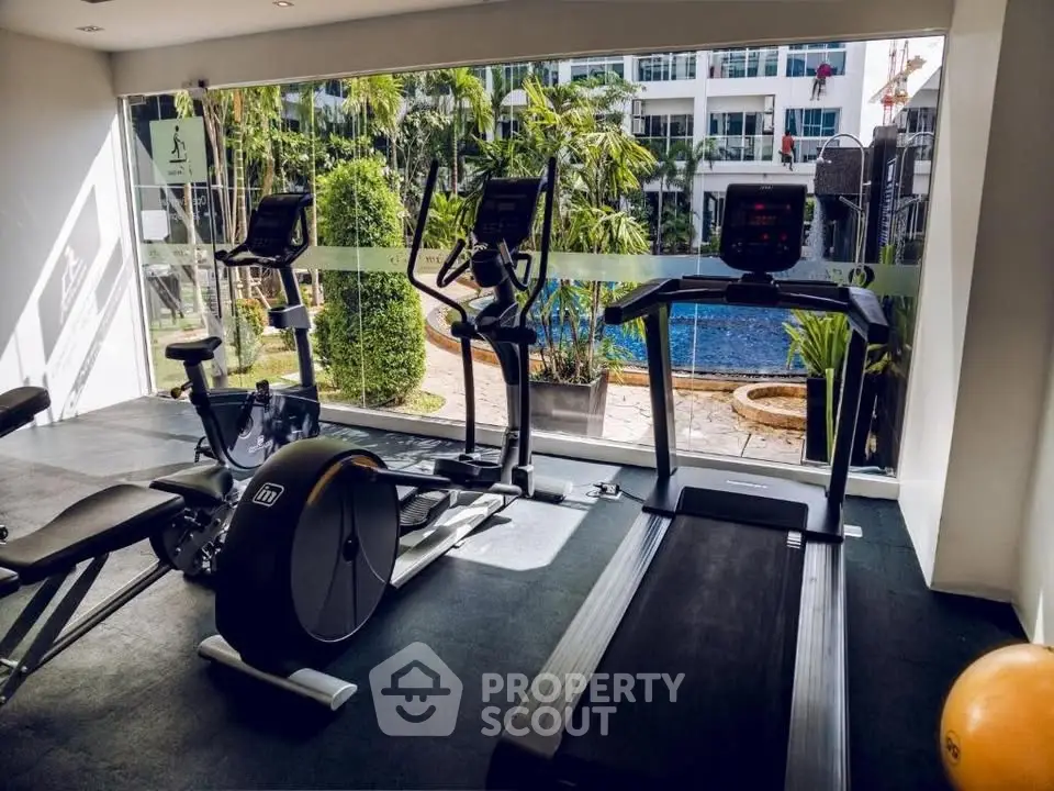 Modern gym with exercise equipment overlooking a pool in a luxury apartment complex.