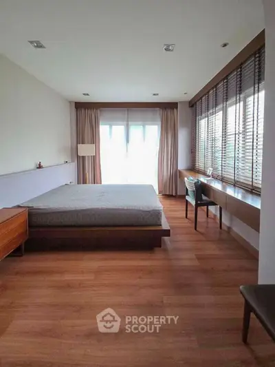 Spacious bedroom with wooden flooring and large windows for natural light.