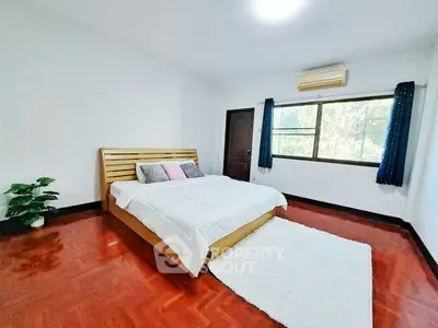 Spacious bedroom with wooden flooring and large window for natural light.