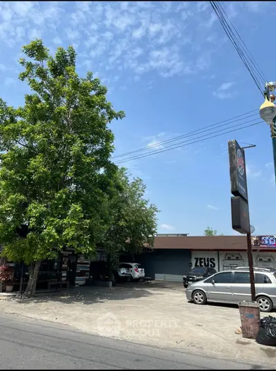 Spacious parking area with tree shade and adjacent building, ideal for commercial use.