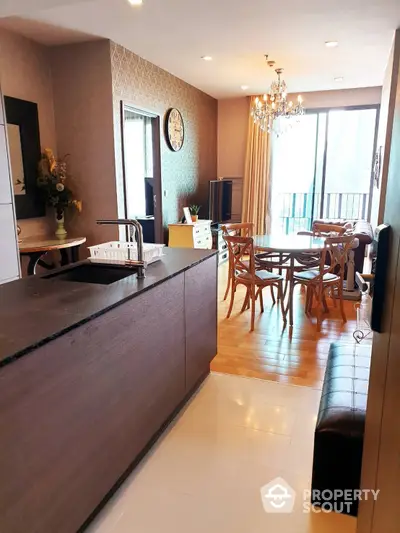 Elegant open-layout kitchen with sleek countertops leading to a cozy dining area, complemented by warm lighting and a classic chandelier, perfect for entertaining.