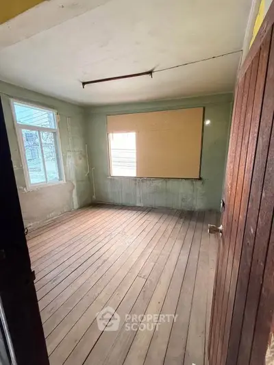 Spacious empty room with wooden flooring and large windows, ideal for renovation.