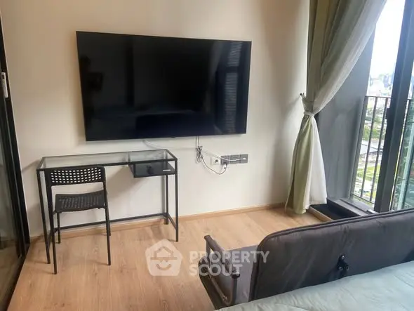 Modern living room with sleek TV, glass desk, and balcony view in stylish apartment.