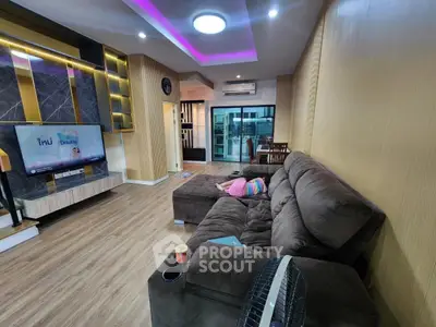 Spacious living room with modern decor and large sofa, featuring ambient lighting and a flat-screen TV.