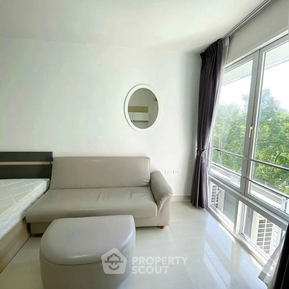 Bright modern living room with large windows and cozy sofa, offering a serene view of greenery.