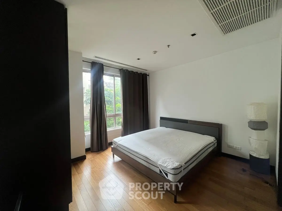 Spacious bedroom with large window and wooden flooring in modern apartment.