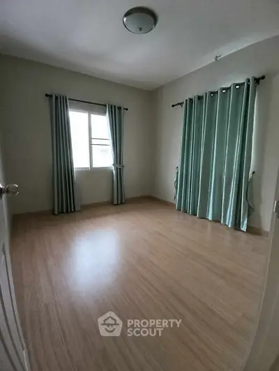 Spacious empty bedroom with wooden flooring and large window with curtains.