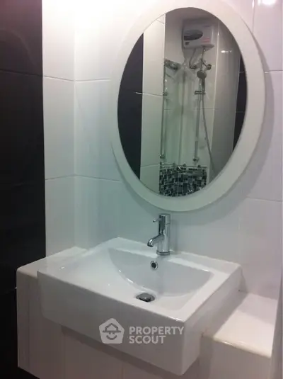 Modern bathroom with sleek white sink and oval mirror, featuring a stylish shower area.