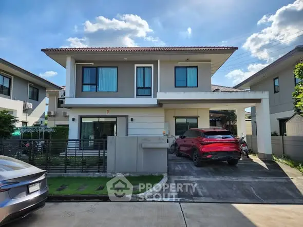 Modern two-story house with driveway and parked cars under a clear blue sky.