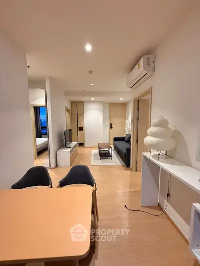 Modern apartment interior with open living and dining area, featuring stylish furniture and wooden flooring.