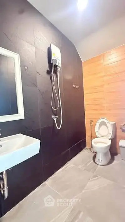 Modern bathroom with sleek black tiles and wooden accents, featuring a shower and white fixtures.