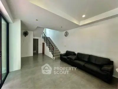 Spacious modern living room with sleek black leather sofas and minimalist staircase design.