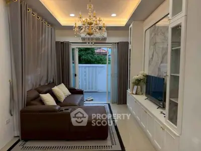 Luxurious living room with elegant chandelier and leather sofa, opening to a serene outdoor view.